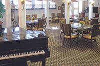 A dining area featuring tables and chairs, with a piano in the foreground.