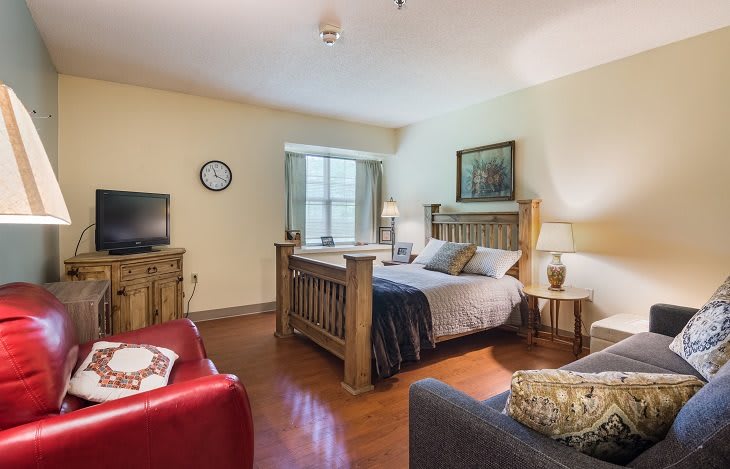 A cozy bedroom featuring a wooden bed, an armchair, and a television.