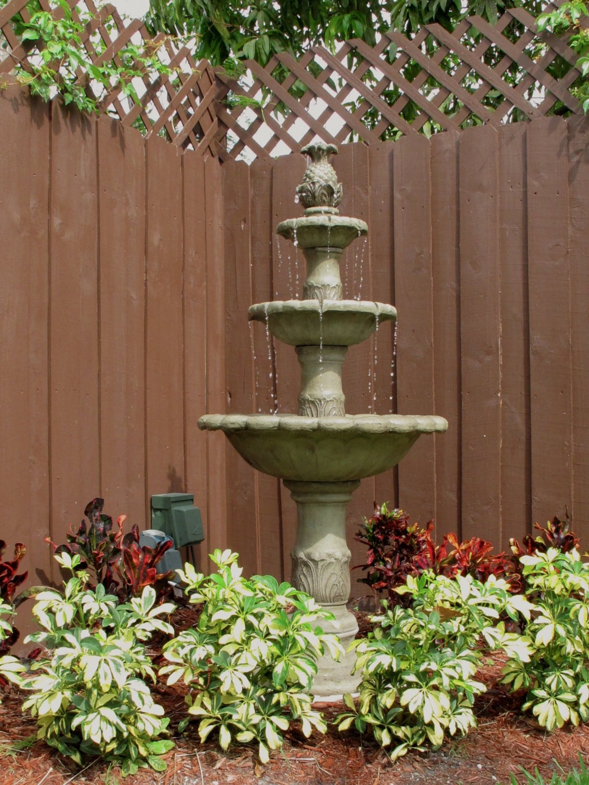 A tiered fountain surrounded by lush plants in a garden setting.