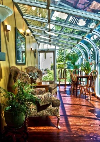 A bright sunroom filled with lush plants and comfortable furniture, featuring a glass ceiling that lets in abundant natural light.
