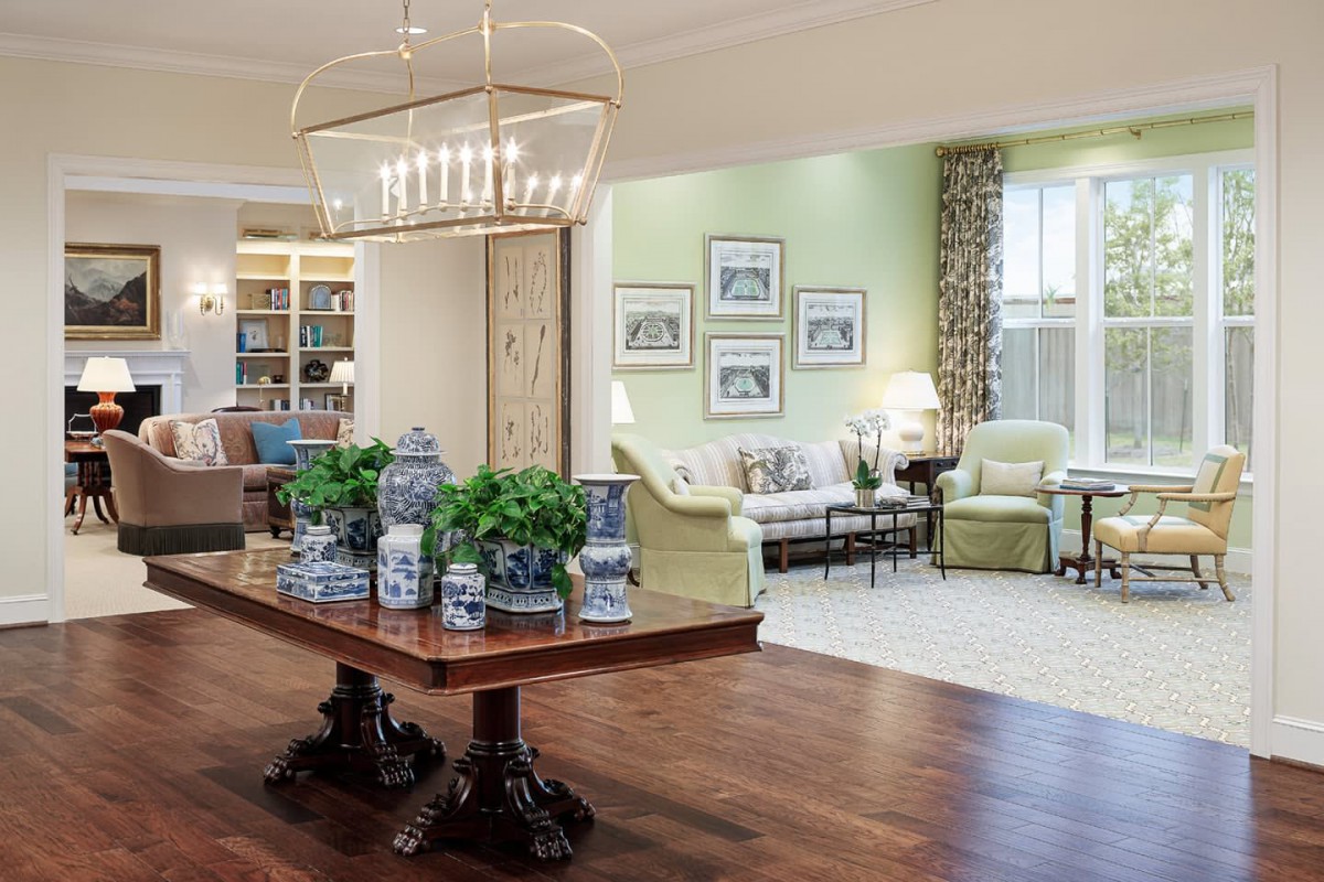 A beautifully designed living room featuring elegant furniture, a grand chandelier, and tasteful decor with potted plants on a hardwood floor.