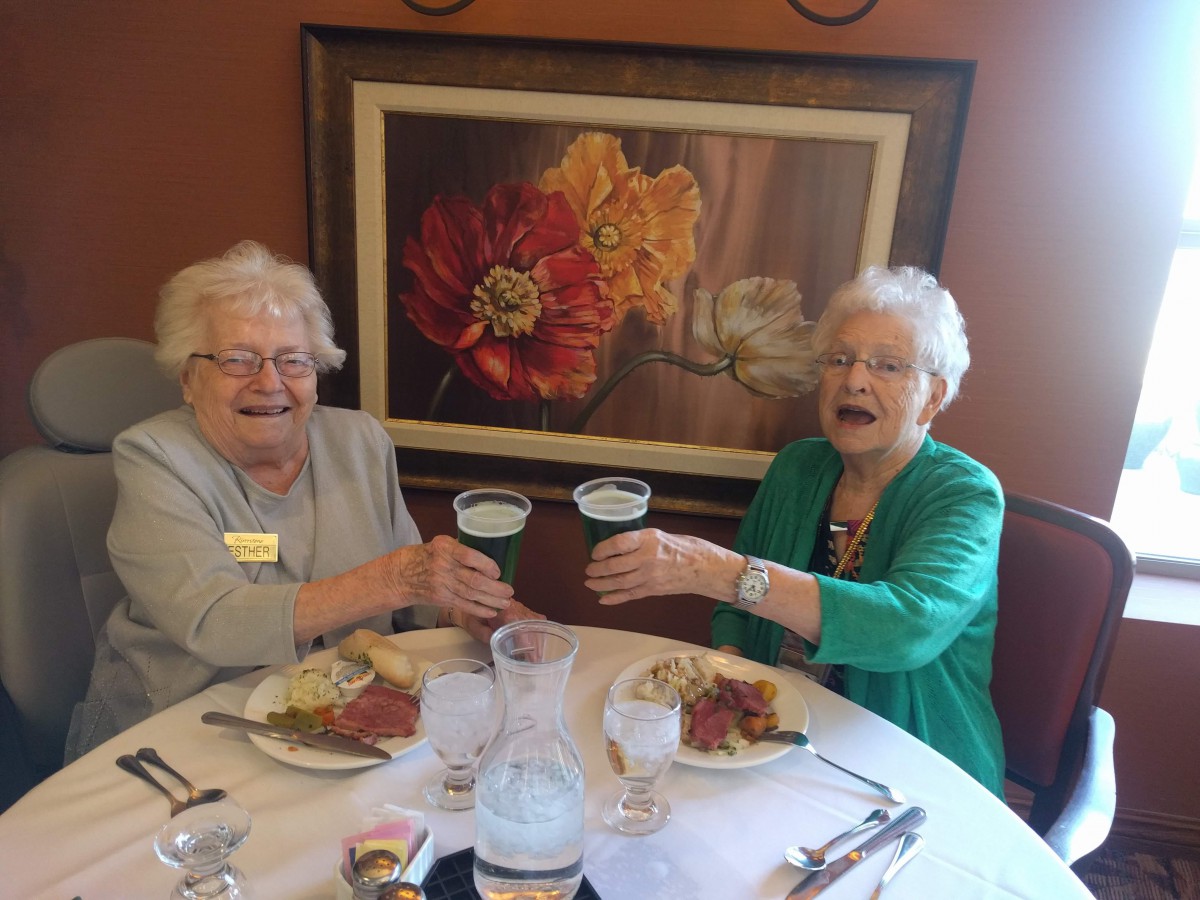 Two elderly women enjoying a meal and raising their glasses in a toast.