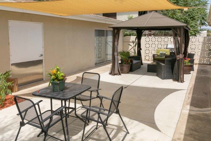 A cozy patio with a shade sail, outdoor seating, and a gazebo offering an inviting space for relaxation.