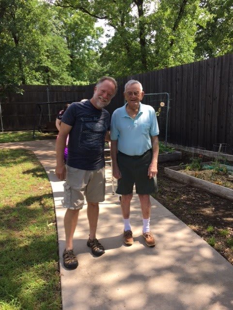 Two people standing on a path in a garden, enjoying a sunny day.