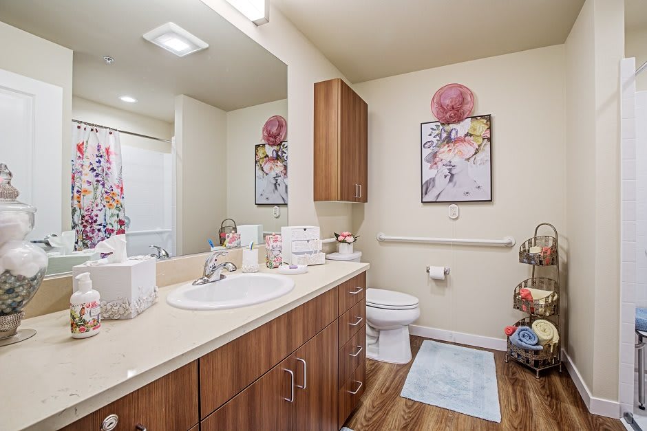 A modern bathroom featuring a wooden cabinet, a sink with various toiletries, and decorative artwork on the walls.