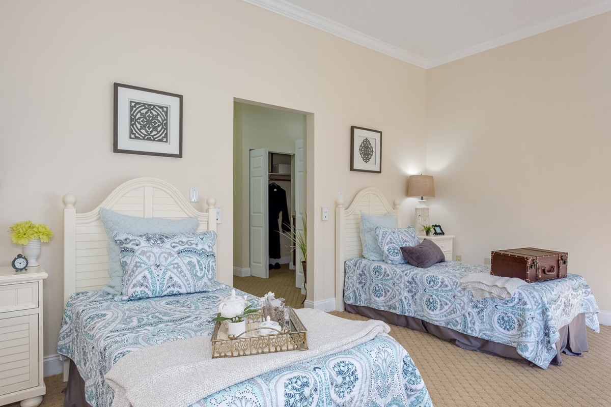 A cozy bedroom with two twin beds featuring blue patterned bedding, complemented by soft lighting and wall art.