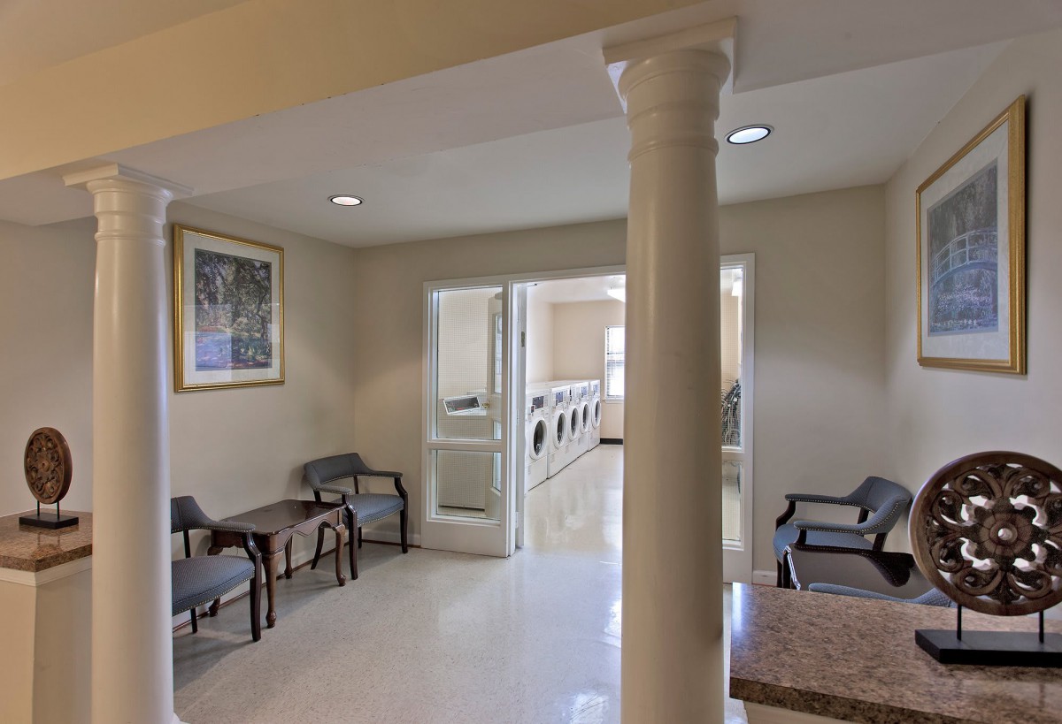 A well-lit laundry room with a waiting area, featuring chairs, tables, and a visible column.