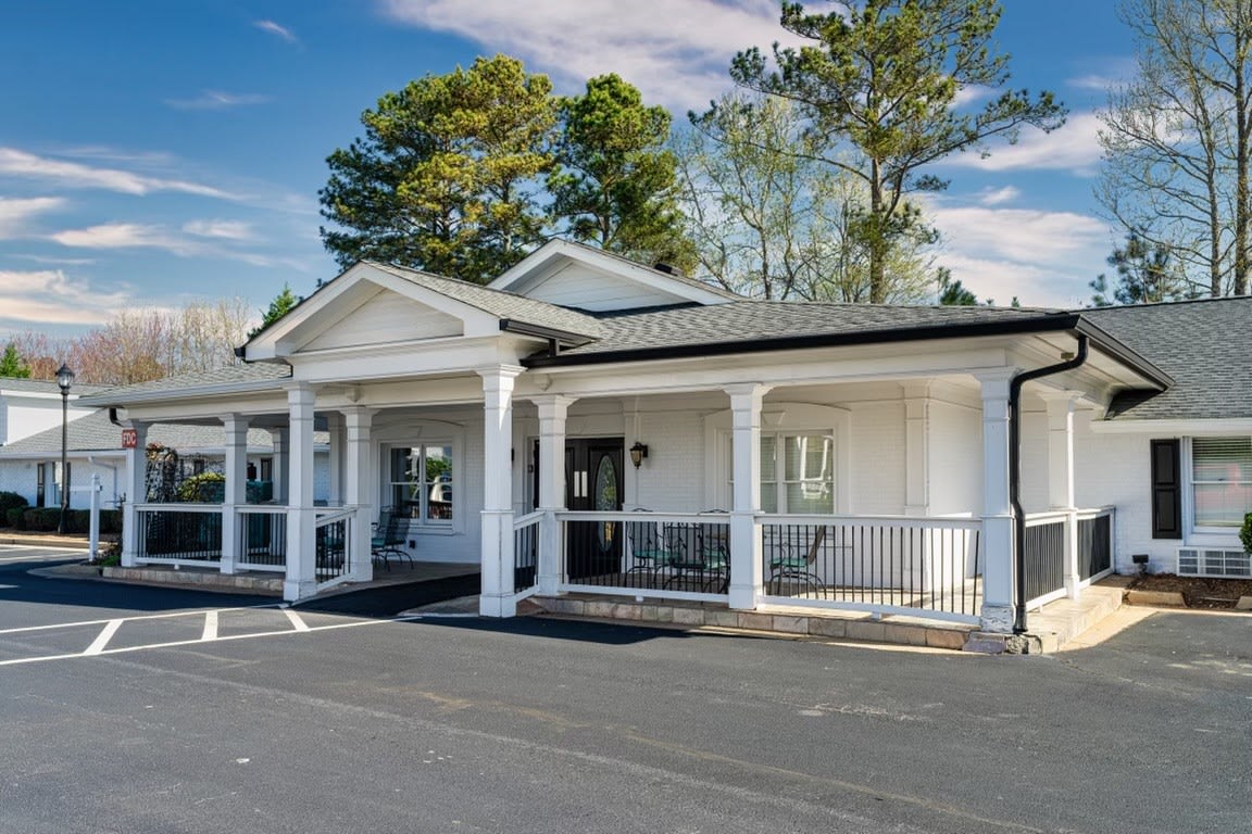 A white building with a porch and columns, surrounded by trees under a clear blue sky.