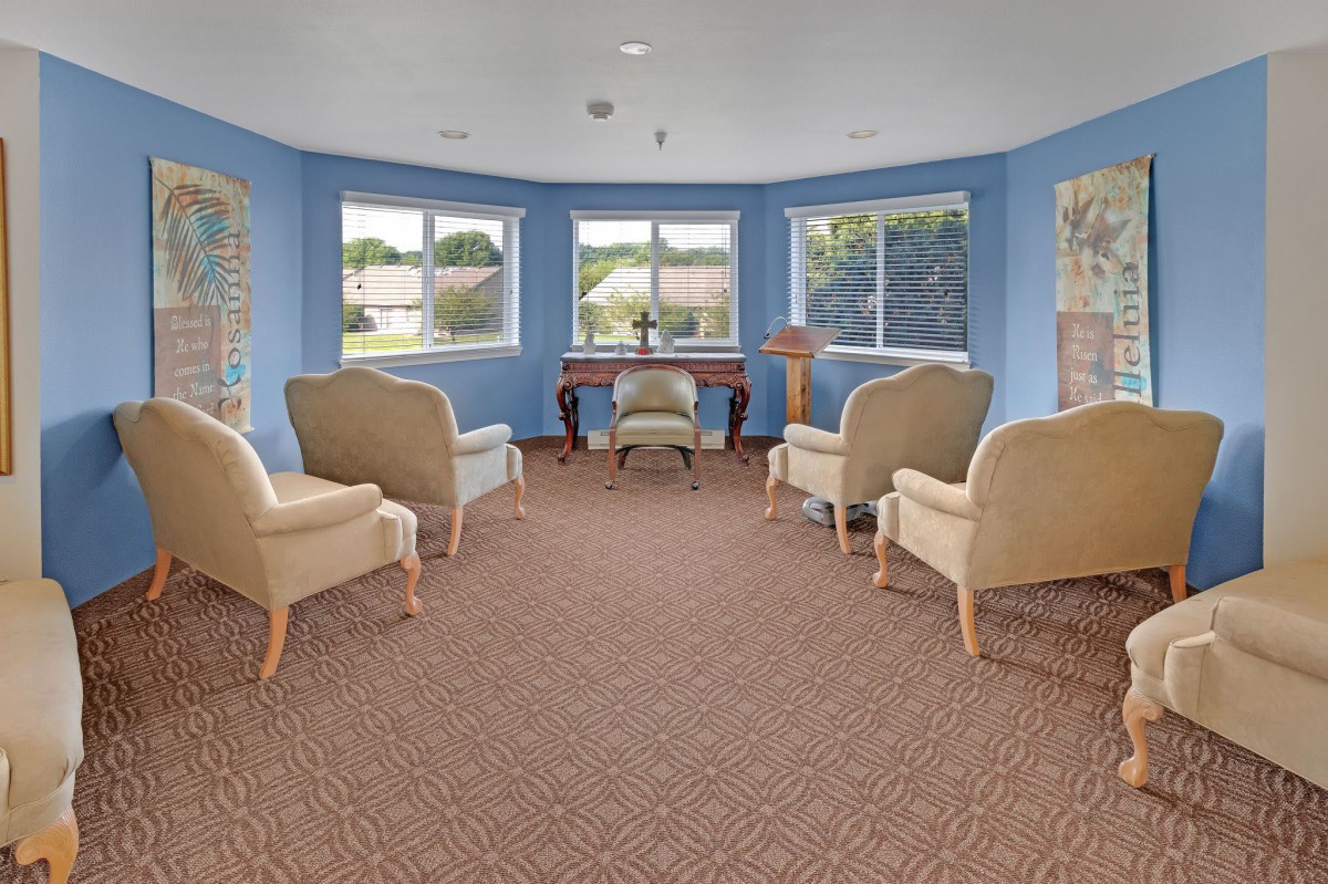 A cozy living room with comfortable chairs and a desk set against blue walls and large windows.