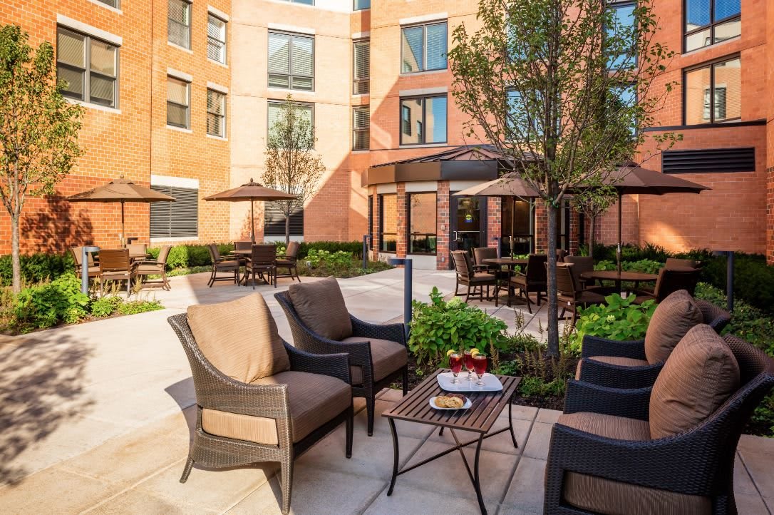A cozy outdoor patio with seating, surrounded by a brick building and greenery.