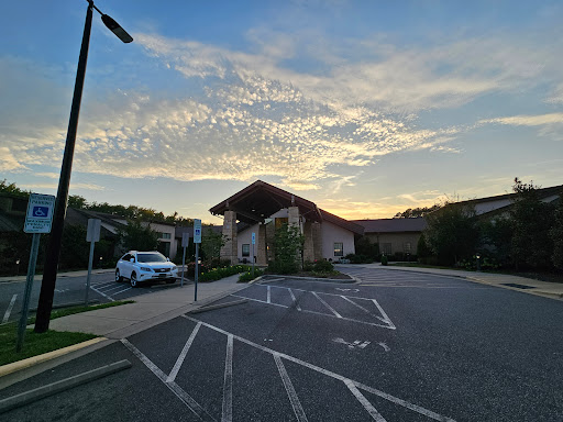 A peaceful sunset over a building, with a clear sky filled with clouds and an empty parking lot.