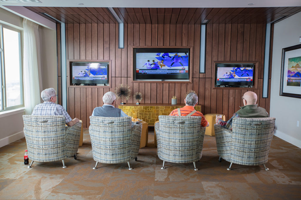 A group of seniors sitting in comfortable chairs, watching multiple televisions indoors.