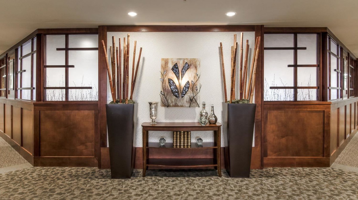 A stylish interior featuring tall vases with decorative sticks, a central wooden console table adorned with books and beverages, and a piece of modern artwork on the wall.
