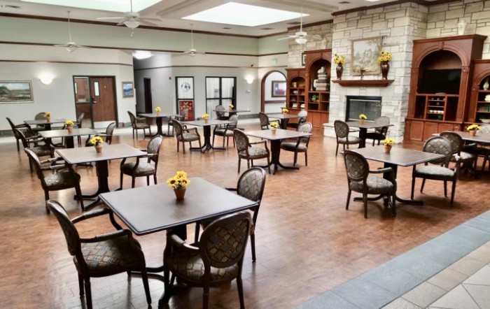 A spacious dining area with tables and chairs, featuring a fireplace and wooden flooring.