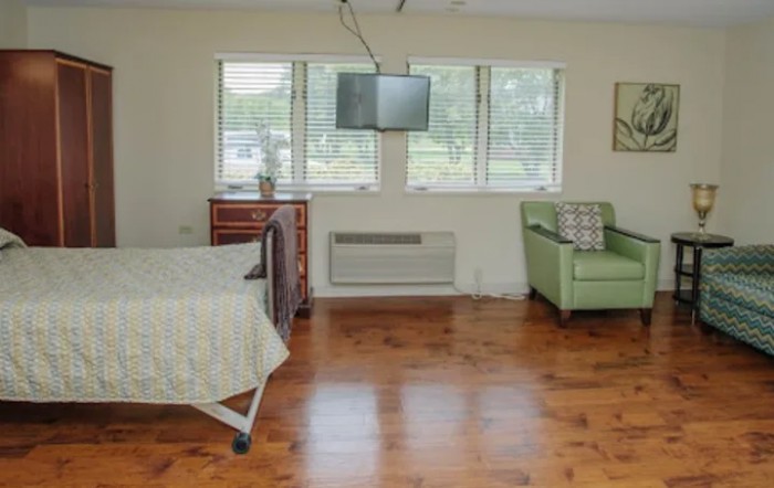 A simple hospital room with a bed, television, and green armchair.