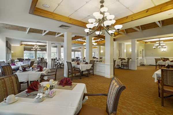 An elegant dining room with neatly arranged tables and chairs, illuminated by chandeliers.