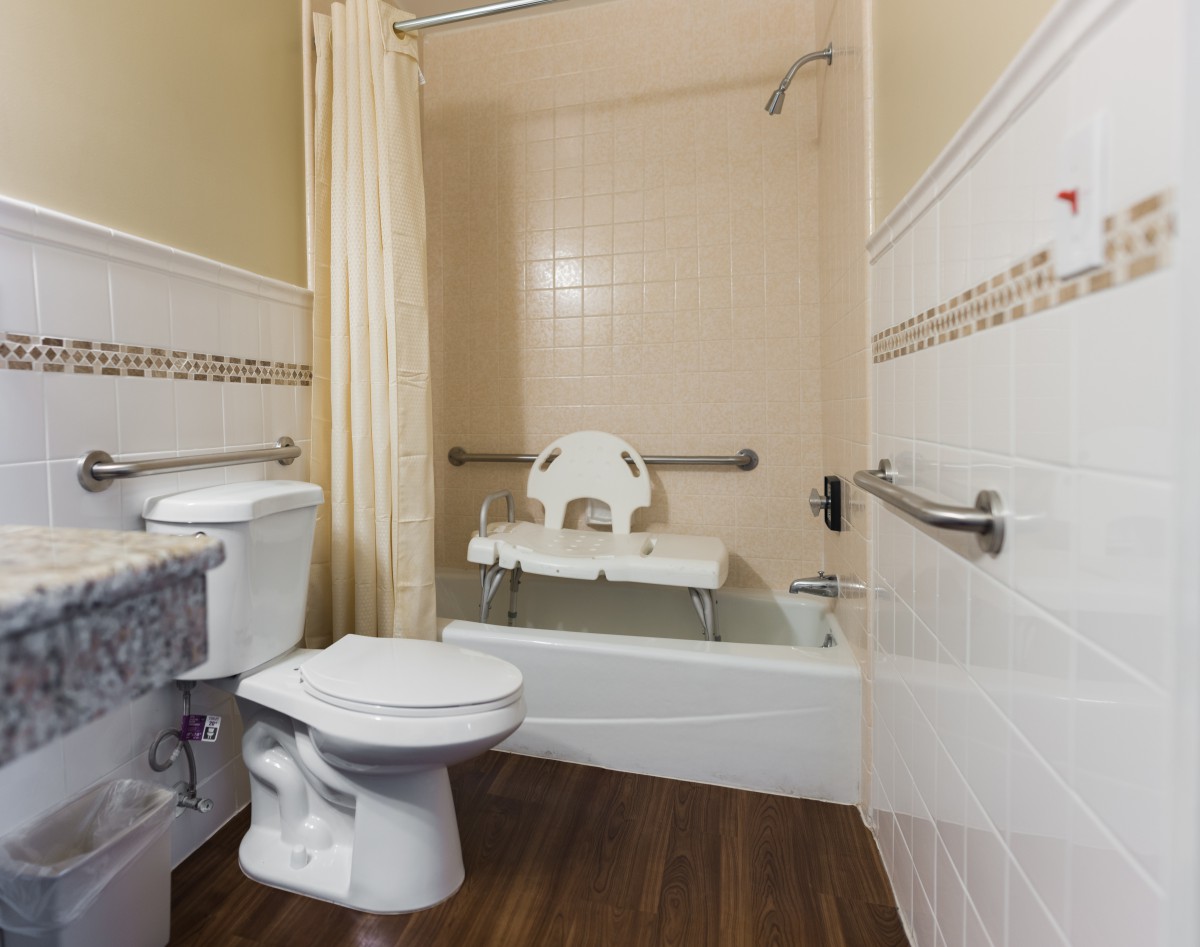 An accessible bathroom with a bathtub equipped with a safety chair and grab bars.