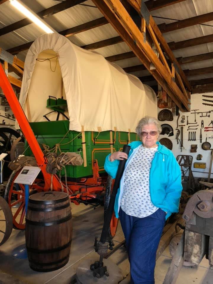 A person standing in a museum next to a historical covered wagon and various artifacts.