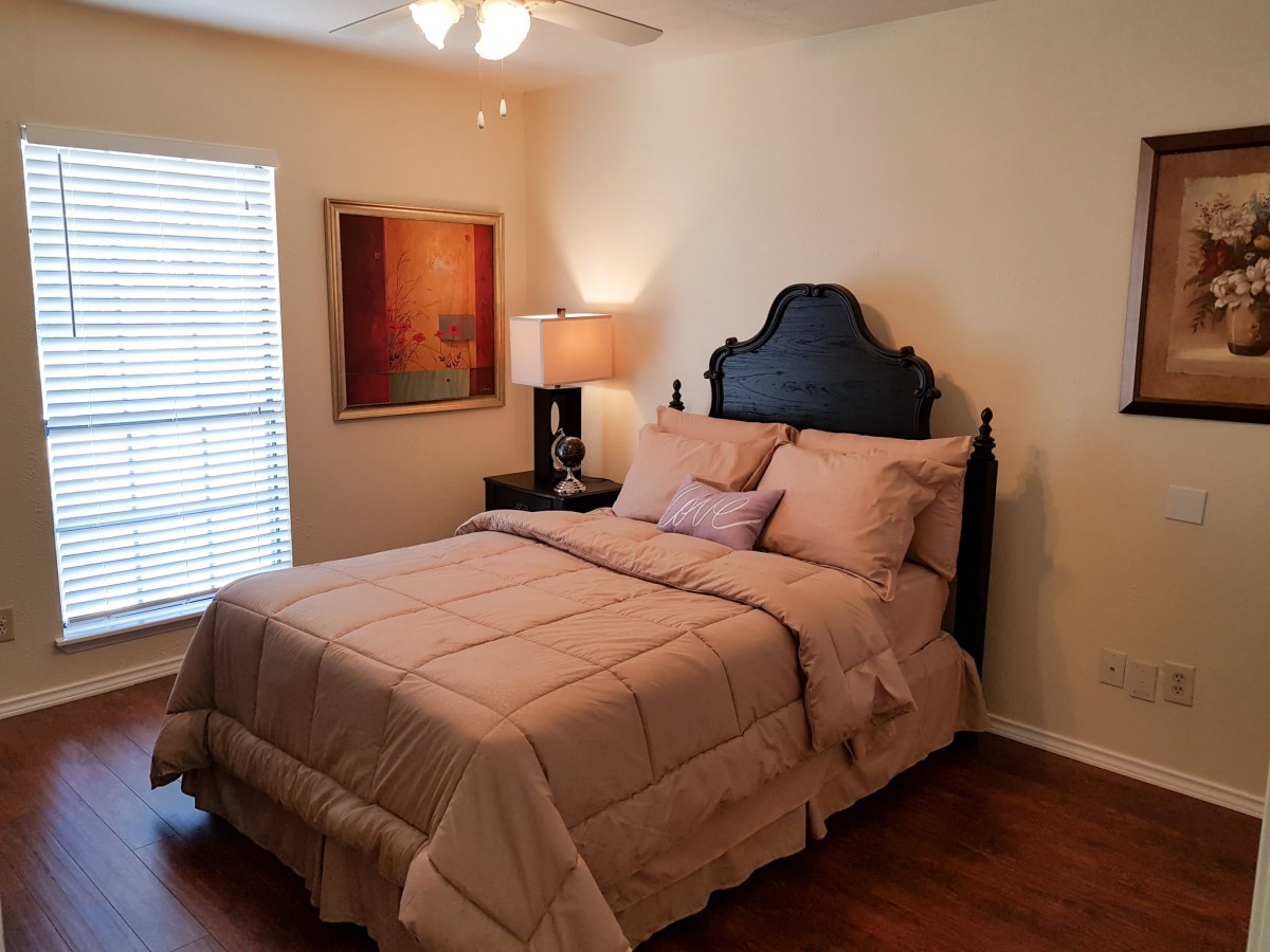 A cozy bedroom with a neatly made bed, bedside lamp, and artwork on the wall.