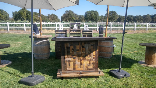 A beautifully arranged outdoor bar setup with a rustic wooden counter and barrels, perfect for an event.