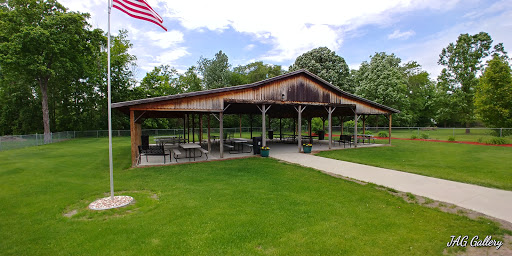 A scenic view of a wooden pavilion with seating, surrounded by lush greenery and an American flag waving in the breeze.