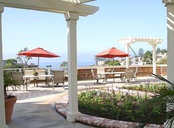 A bright and inviting patio with red umbrellas, offering a stunning ocean view and lush garden surroundings.
