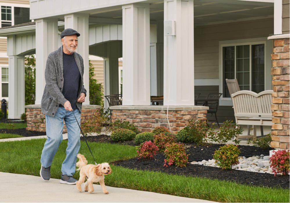A man walking his dog on a sidewalk in front of a house.