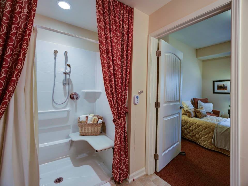 A cozy bathroom with an accessible shower and red curtains, adjacent to a comfortable bedroom.