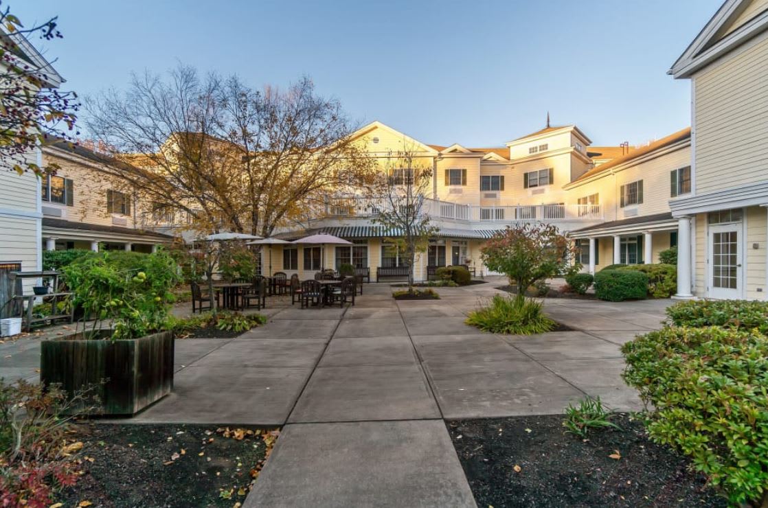 A residential building with a courtyard featuring patio furniture and surrounding trees.