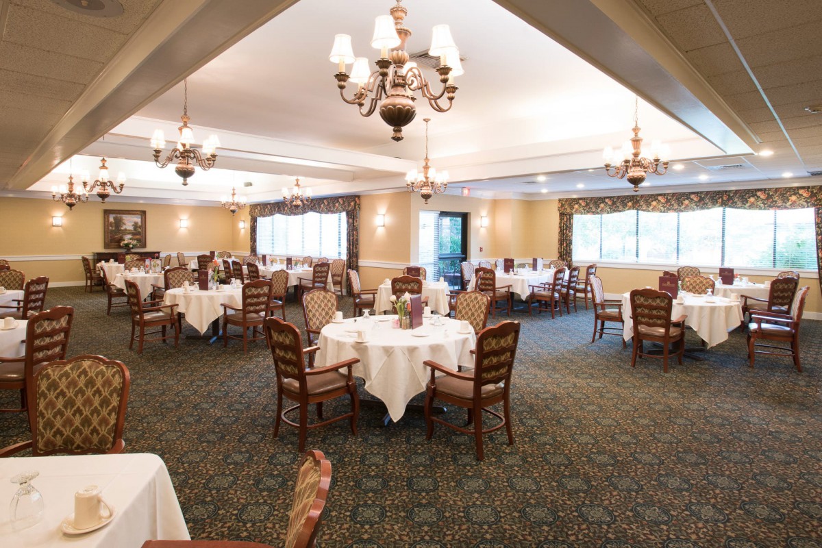 An elegant dining room with neatly arranged tables and chairs, adorned with chandeliers.