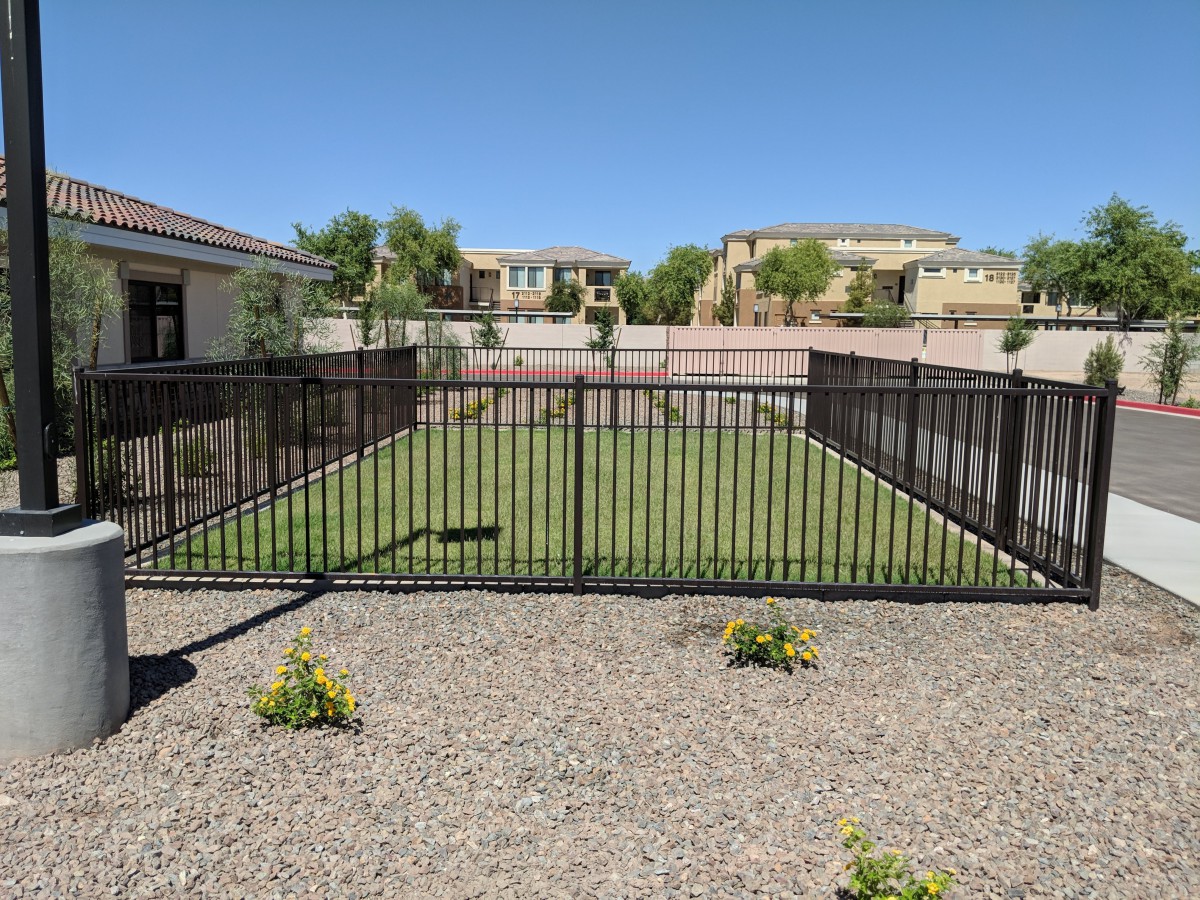 A fenced backyard with a small garden surrounded by a rocky landscape and residential houses in the background.