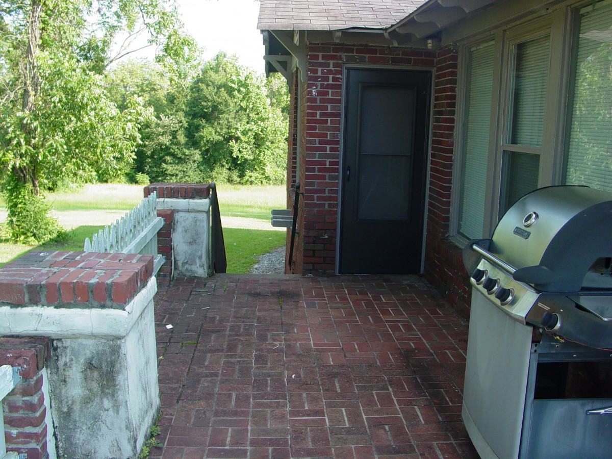 A backyard patio with a brick floor and a grill next to a door.