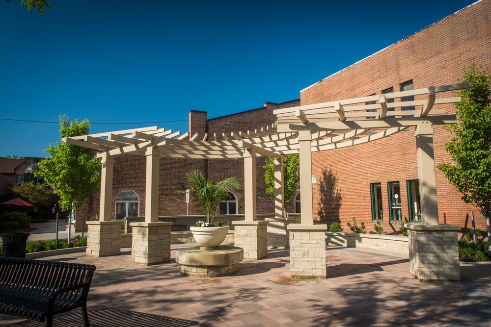 A peaceful courtyard featuring a pergola and a fountain in front of a brick building.