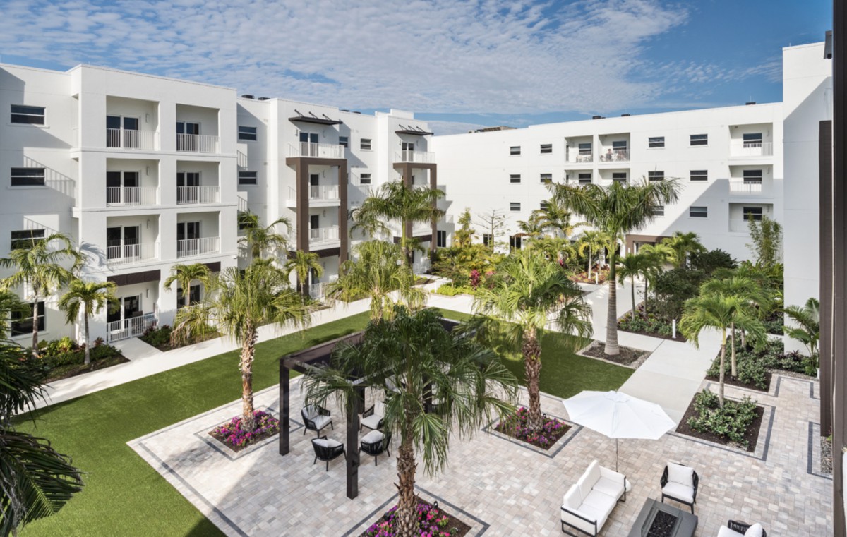 A modern apartment complex featuring a landscaped courtyard with palm trees and outdoor seating.