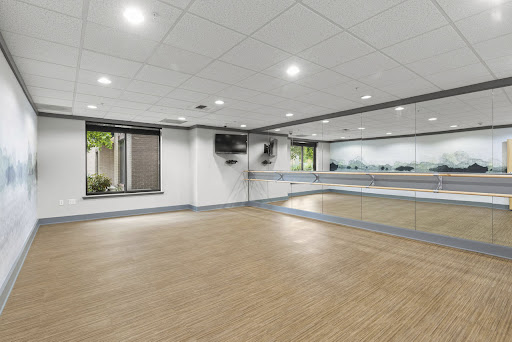 A spacious dance studio featuring a large mirror, bright lighting, and a wooden floor, ideal for practice and classes.