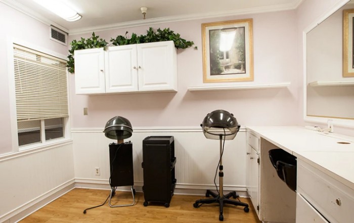 A cozy hair salon interior featuring hair dryers, chairs, and white cabinetry against soft-colored walls.