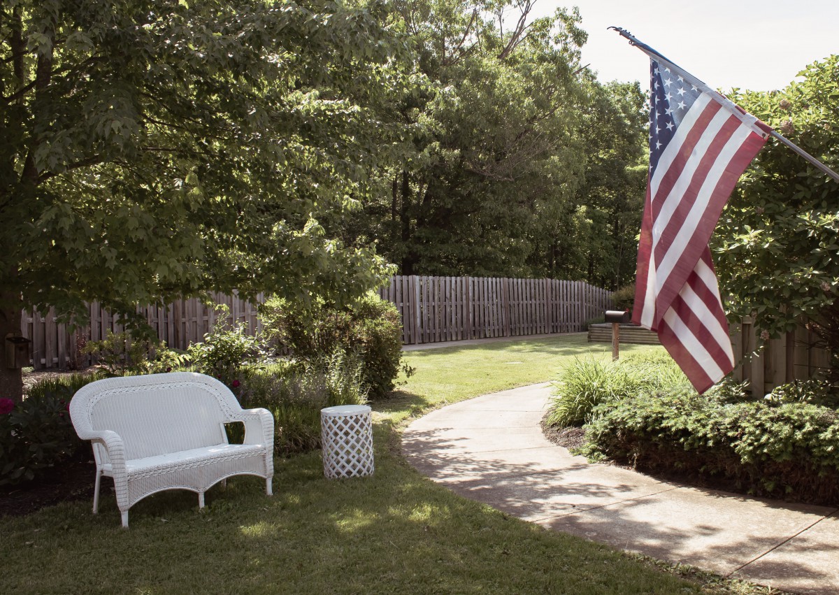 A peaceful backyard scene with a white bench and an American flag.
