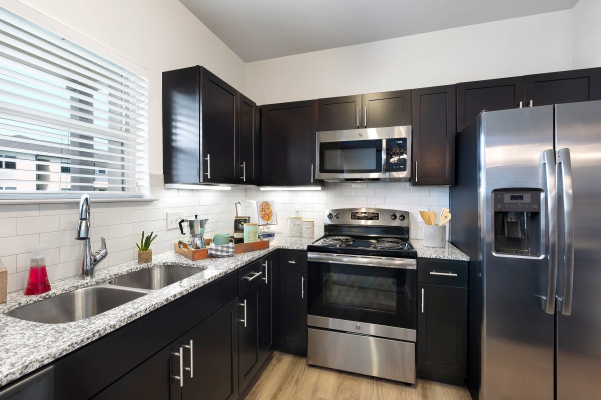 A modern kitchen with dark cabinets and stainless steel appliances.