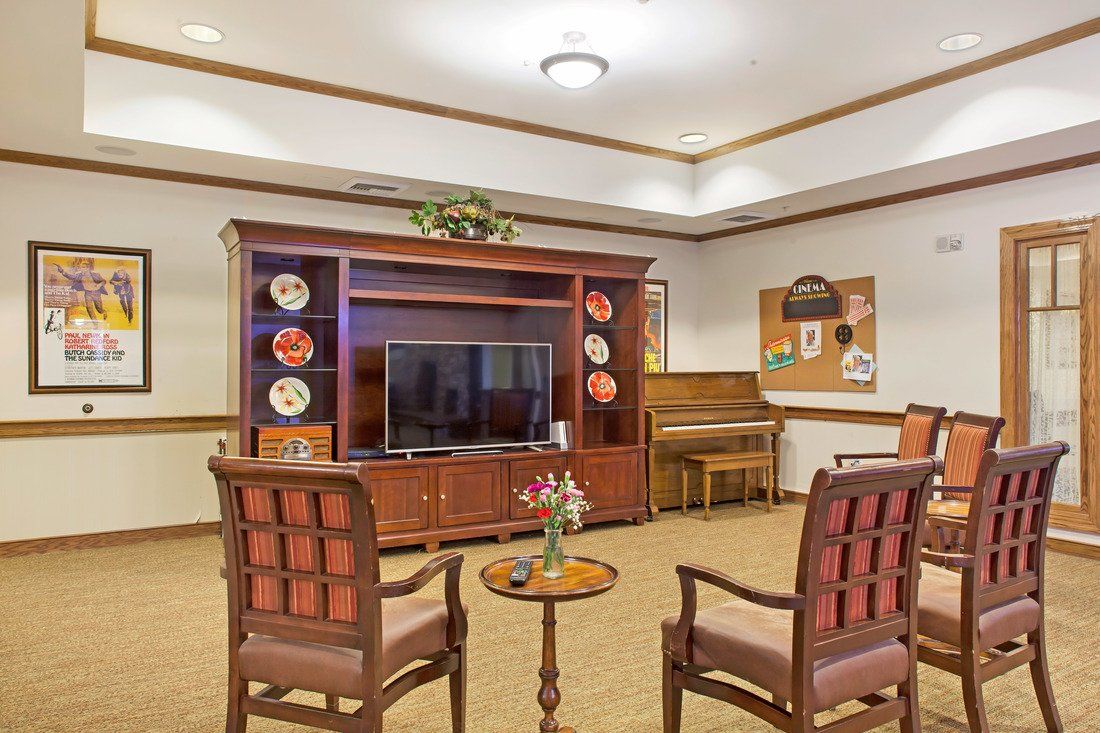 A cozy living room featuring a wooden entertainment center, a television, chairs, and a piano.