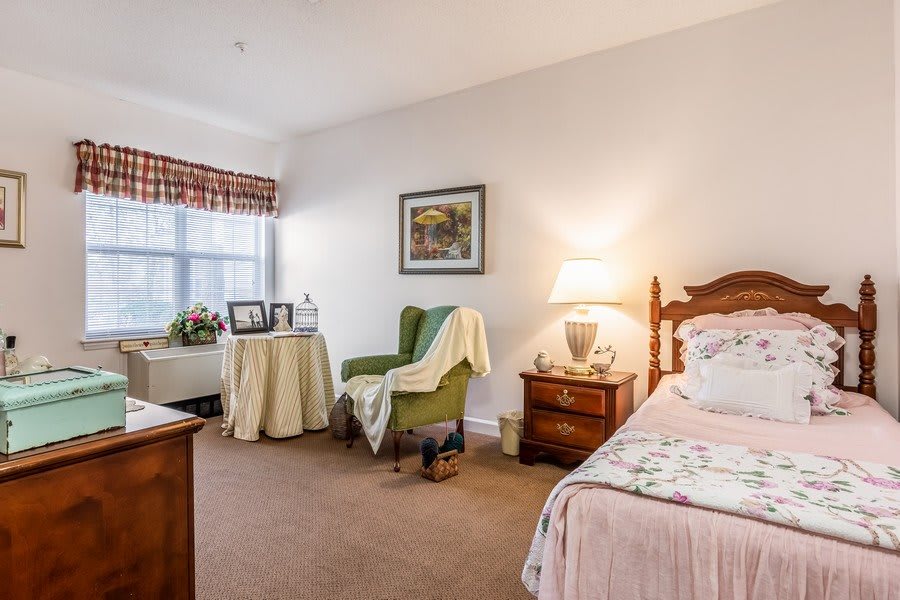 A cozy bedroom with a comfortable bed, an armchair, and a side table beside a softly glowing lamp.