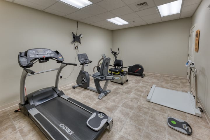 A small gym with various exercise equipment including a treadmill, stationary bike, and elliptical machine.
