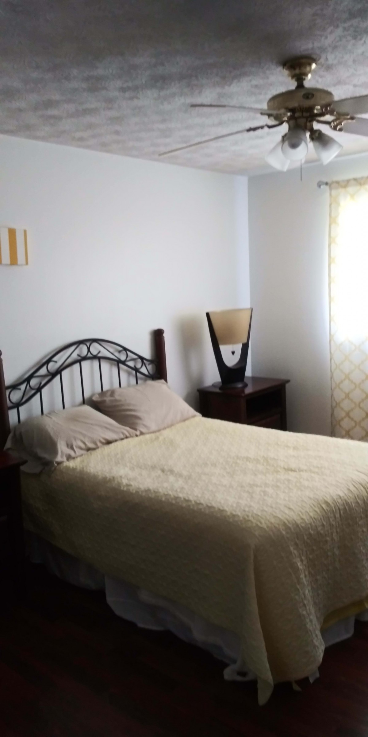 A cozy bedroom with a metal-framed bed, side table, and lamp beside a window.