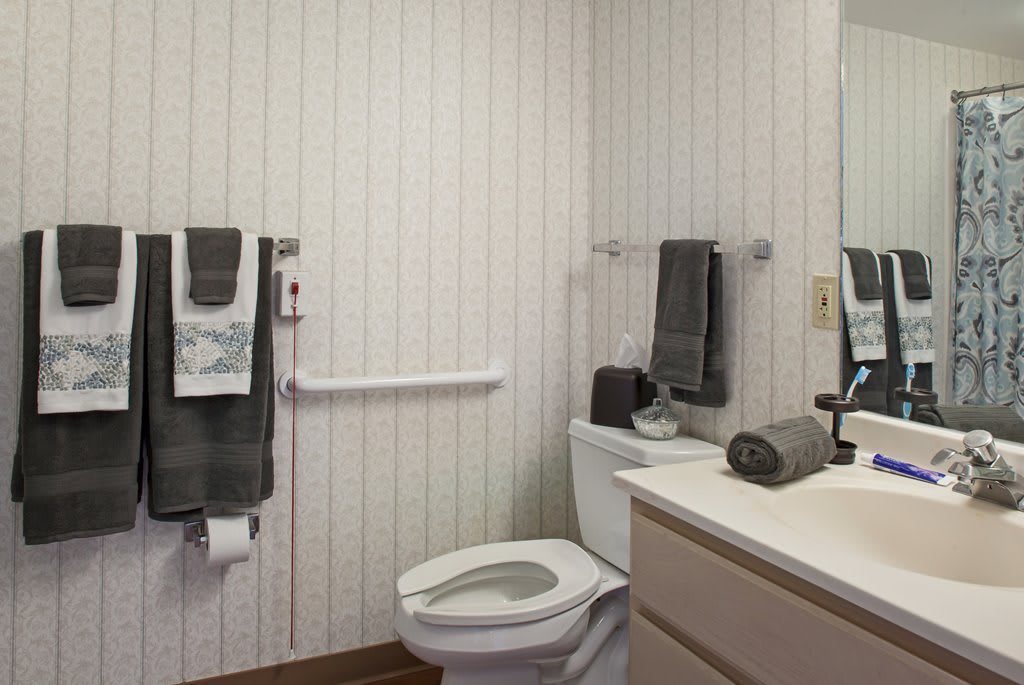 A compact bathroom with a toilet, sink, and neatly arranged towels against a paneled wall.