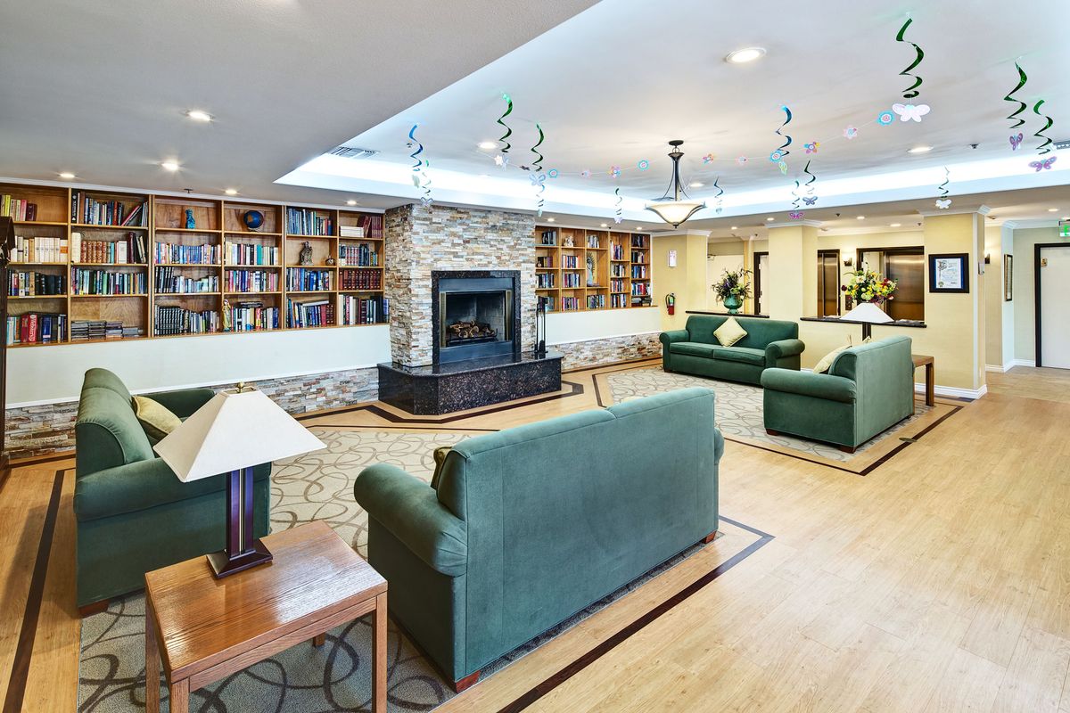 A cozy living room with a fireplace and bookshelves, featuring comfortable sofas and elegant chandeliers.