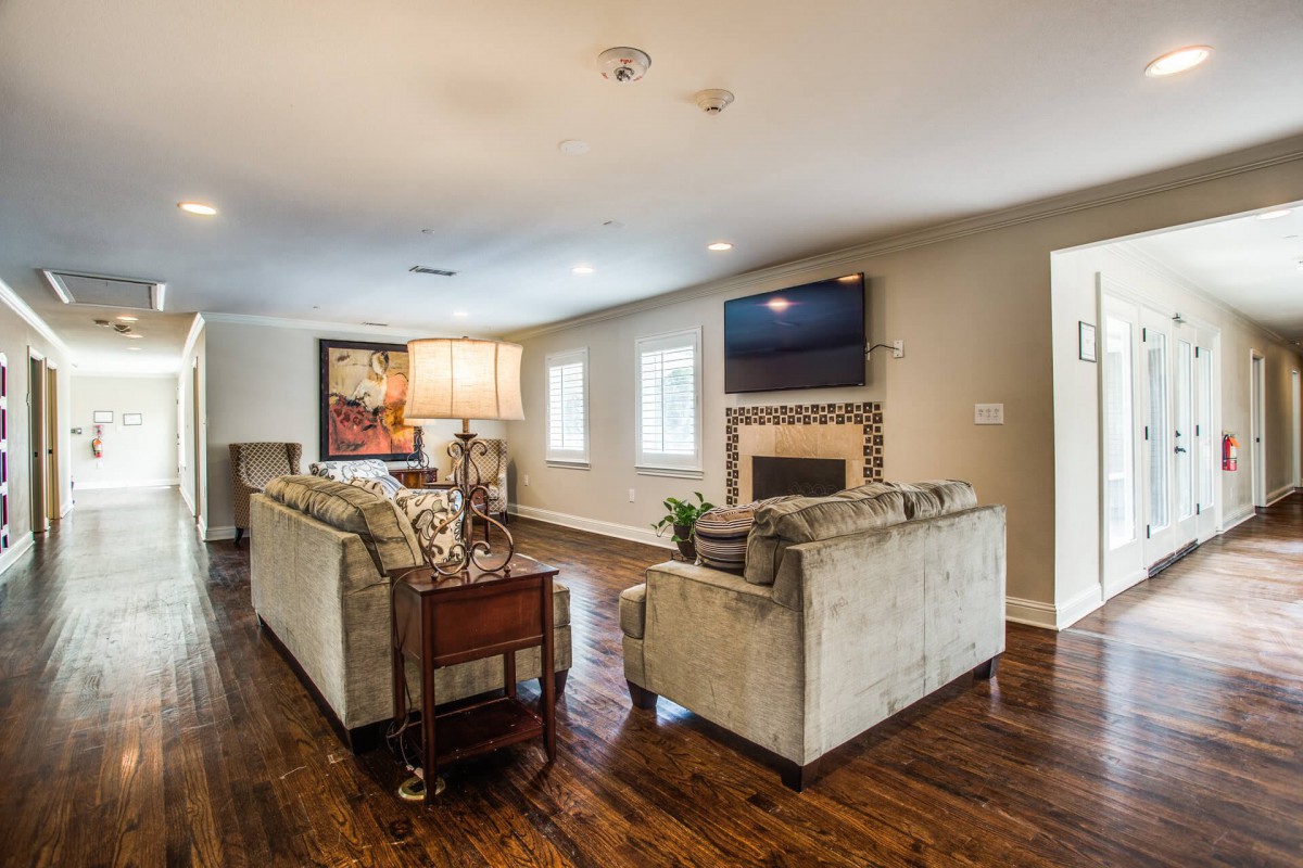A spacious and well-lit living room featuring a cozy sofa, a modern fireplace with a television above it, and elegant hardwood floors.
