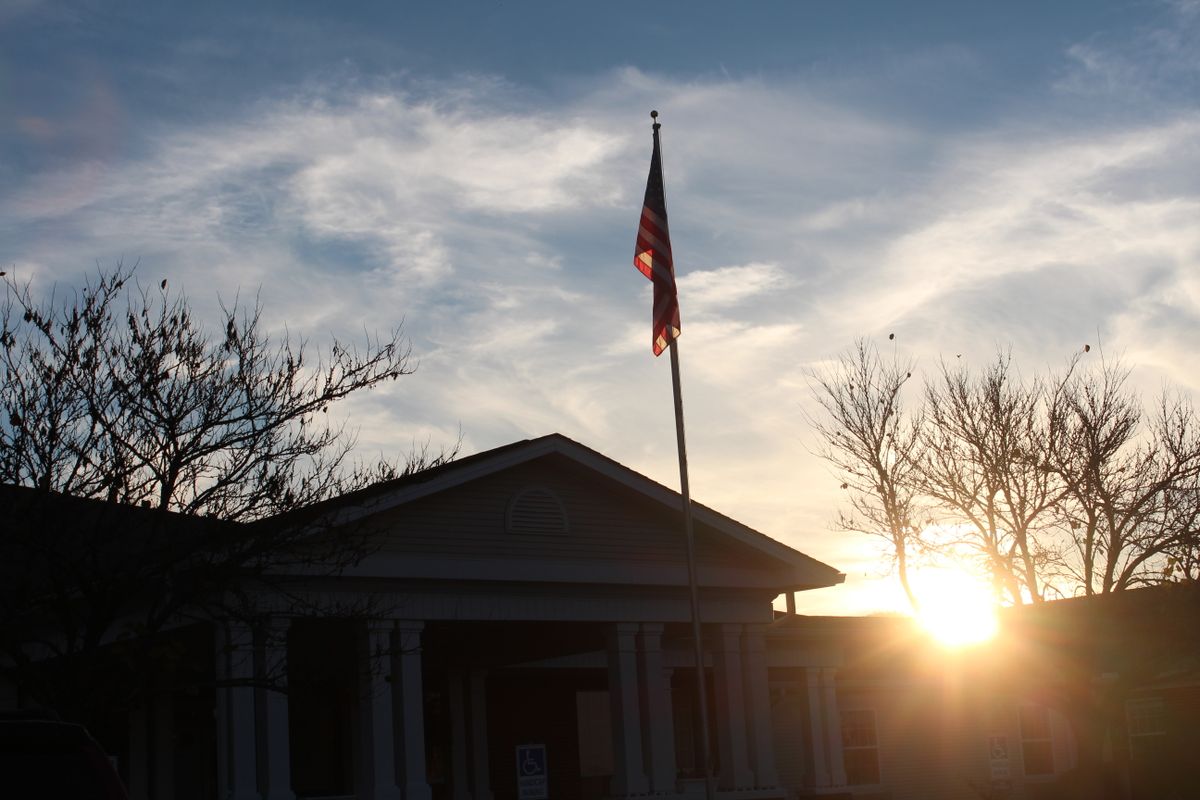A flag atop a building silhouetted against a sunset sky.