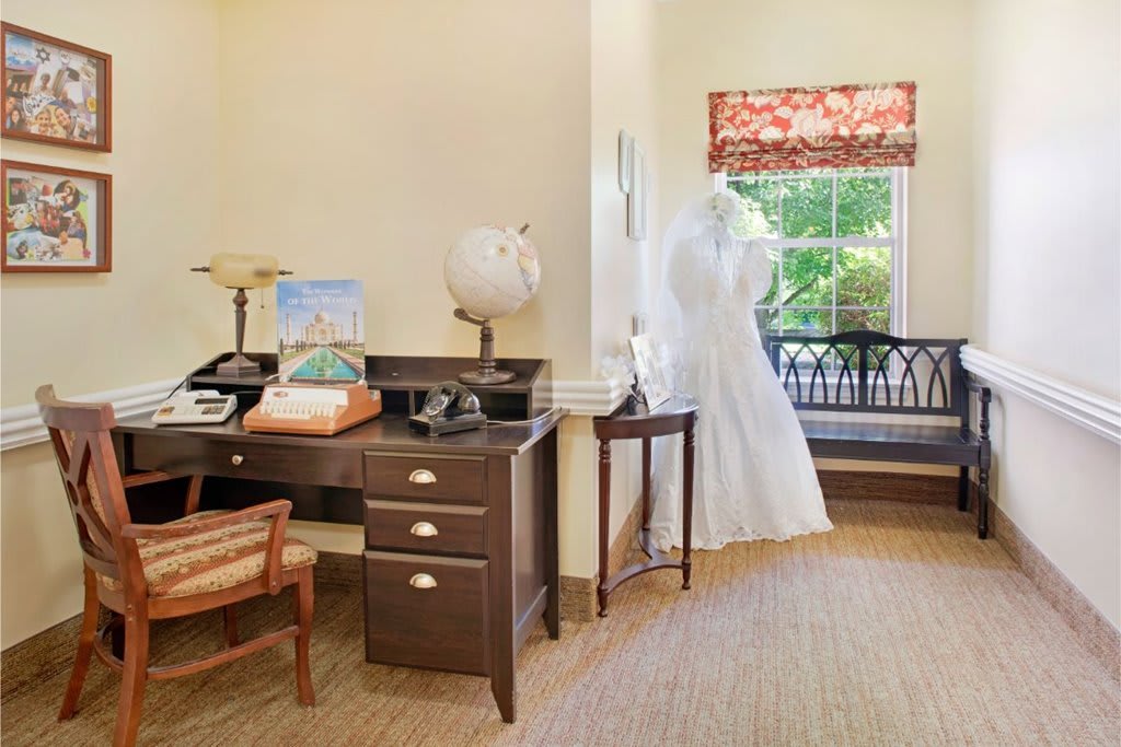 A vintage-style office with a desk featuring a typewriter, telephone, and globe, alongside a dress form by the window.