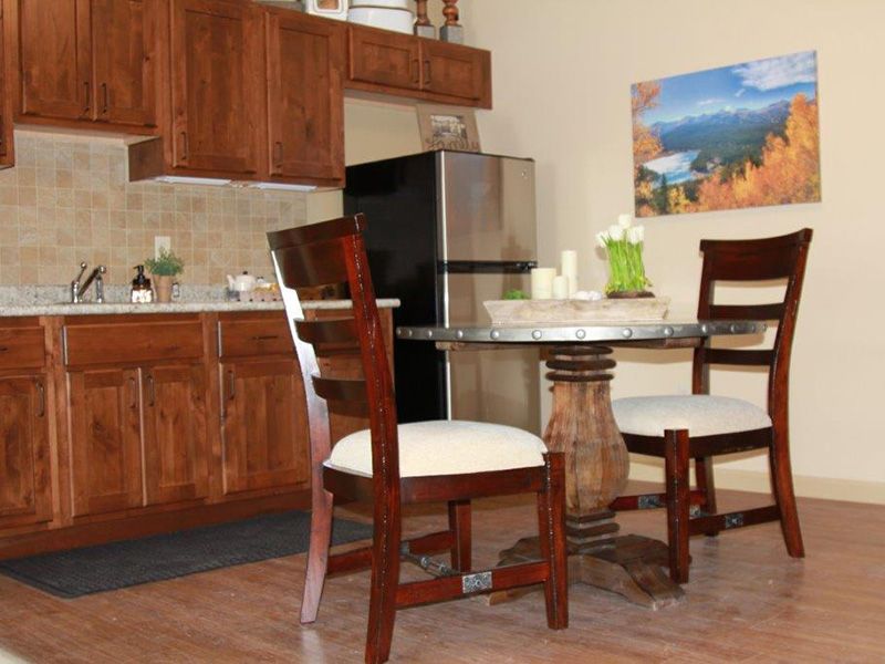 A modern kitchen with wooden cabinetry and a dining area featuring a round glass table and cushioned chairs.