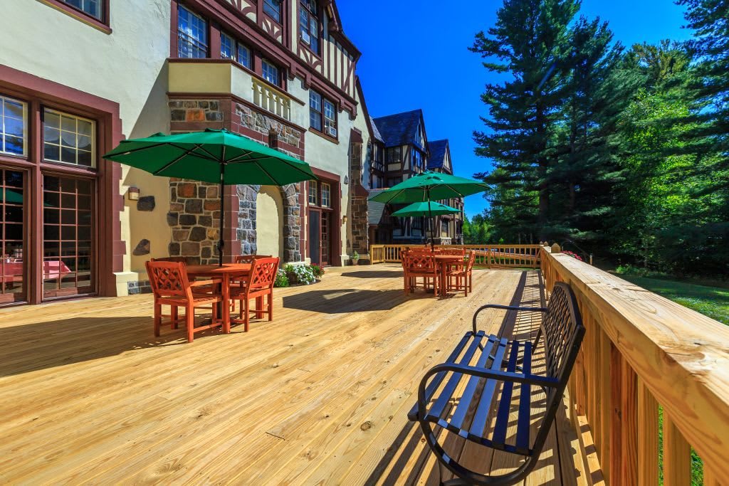 A spacious wooden deck with tables, chairs, and umbrellas outside a building on a sunny day.