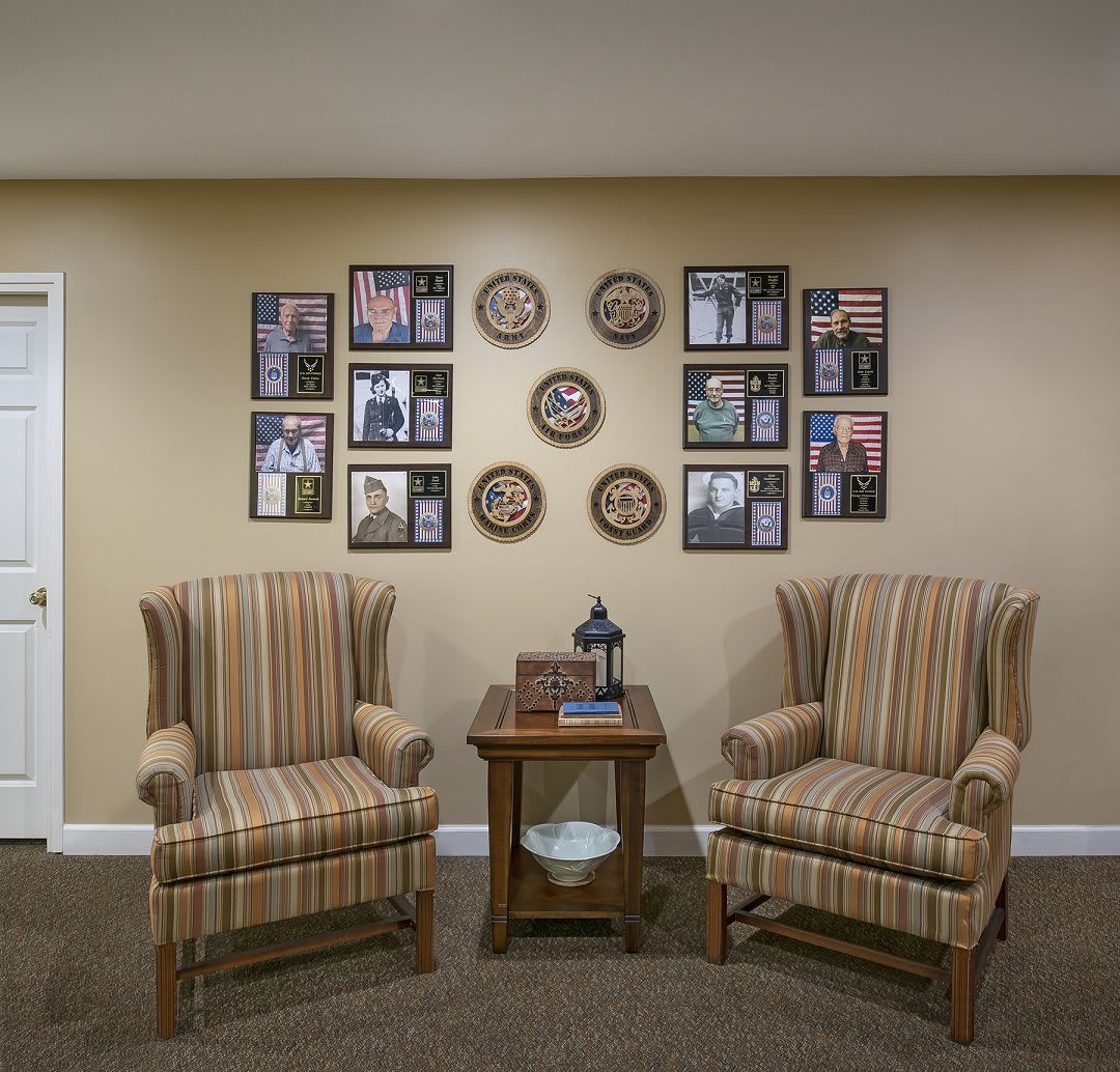 A cozy seating area featuring two striped armchairs flanking a wooden side table, with family photographs and decorative plates adorning the wall.